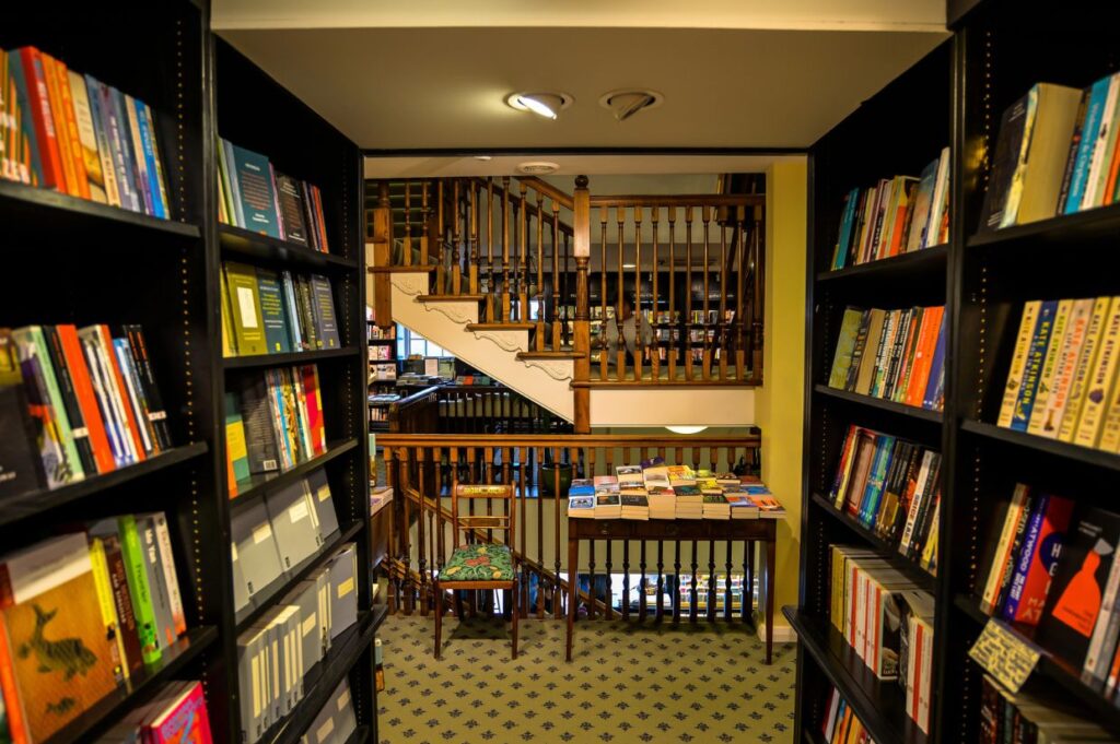 A cozy bookshop interior with black bookshelves filled with colorful books on both sides of a narrow aisle.