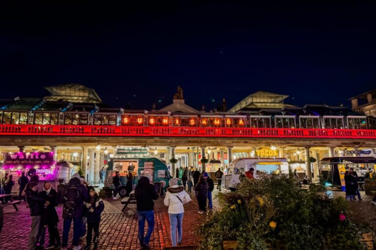 A lively night scene at Covent Garden in London, featuring illuminated food trucks and market stalls surrounded by people.
