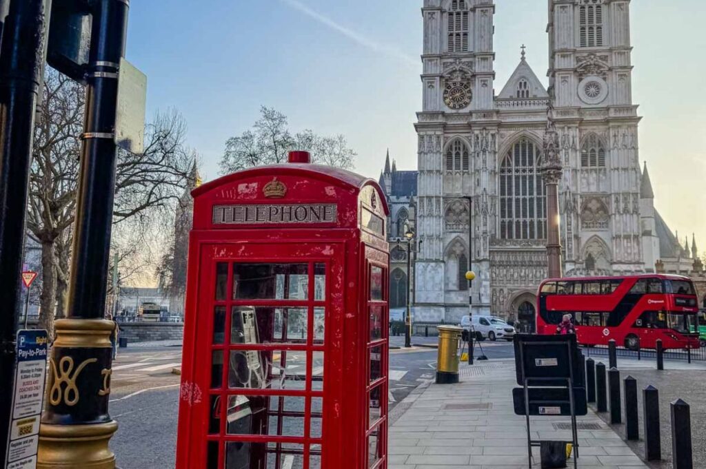 A classic red telephone box stands in the foreground with Big Ben and the Houses of Parliament rising in the background, symbolizing iconic London.