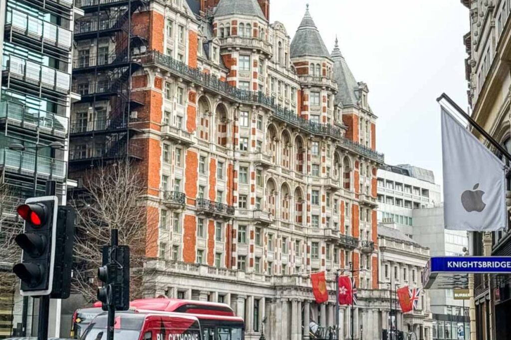 Sicilian Avenue in London is captured with its grand Edwardian-style red-and-white brick buildings, featuring arches, columns, and detailed balconies along a lively street.