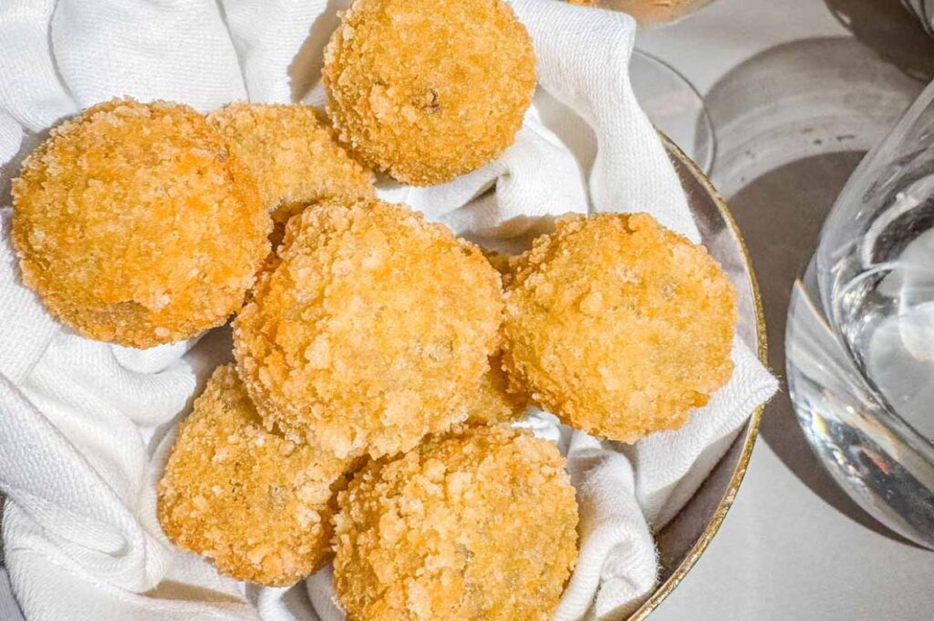 Crispy breaded balls served in a bowl beside a glass of white wine with ice.