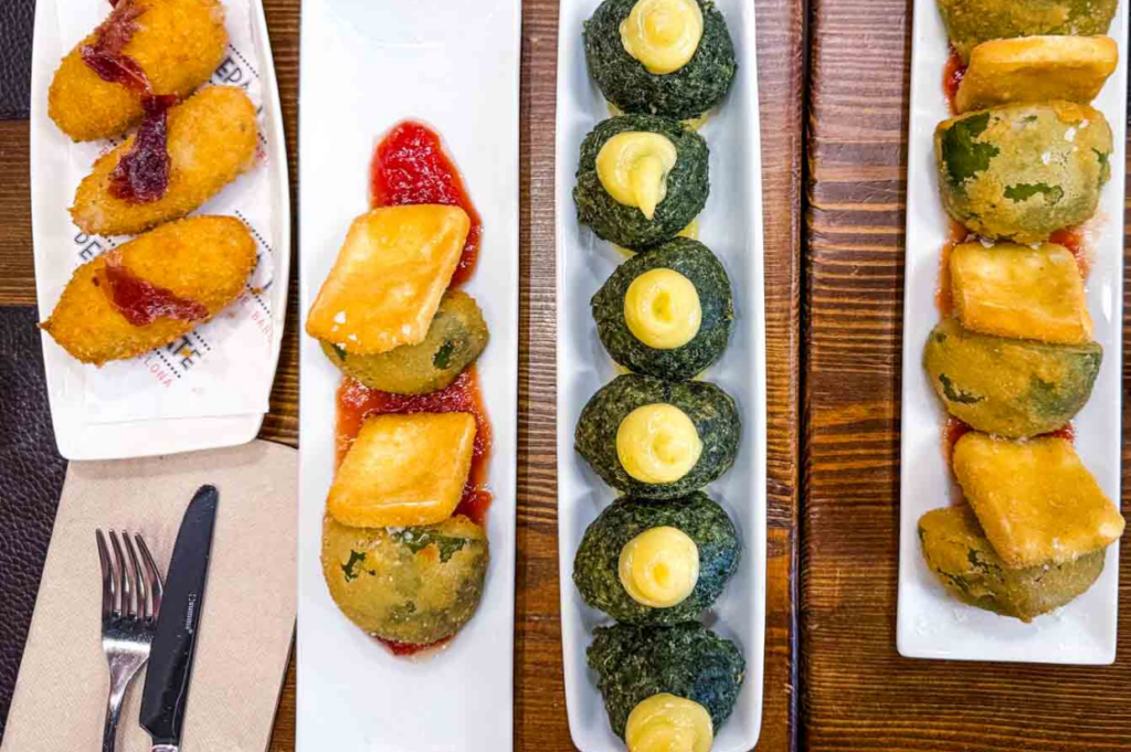 Four rectangular plates display various fried foods on a wooden table. Each has colorful garnishes, creating an inviting and vibrant culinary presentation.