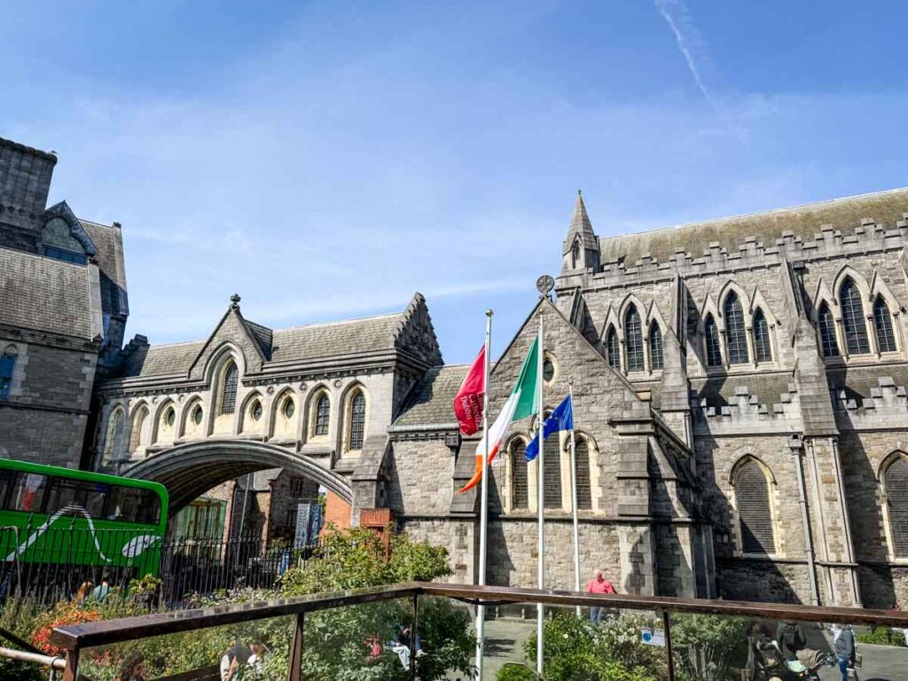 Christ Church Cathedral in Dublin, Ireland, with its Gothic stone architecture, arched bridge, and flags flying in front on a sunny day.