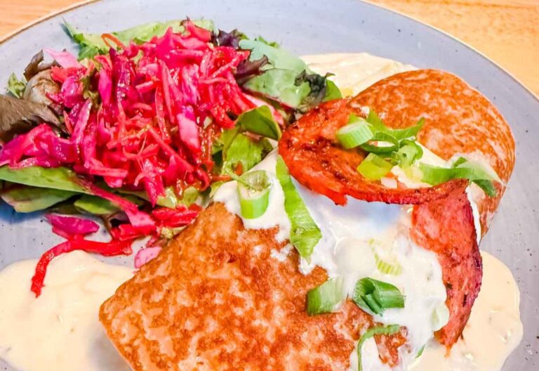 A savory crepe topped with sauce, green onions, and tomato slices sits next to a vibrant salad of mixed greens and shredded red cabbage.